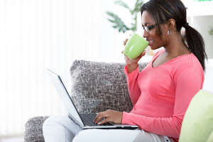 Black woman using a laptop while having a tea in her living room